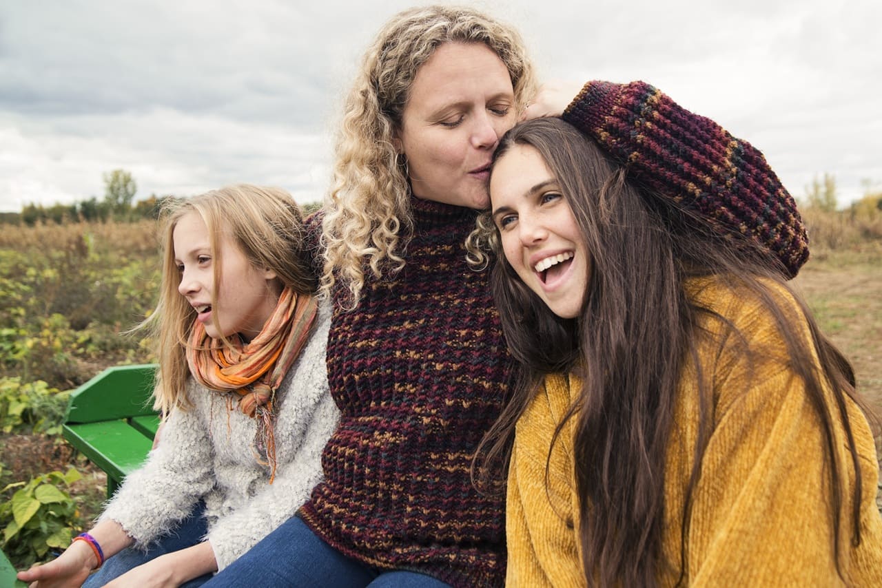 Mother kissing teenage daughter strolling in trailer in field
